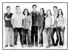 Portretfoto familie van neven en nichten staand tegen muur met 8 personen in zwart-wit gefotografeerd in fotostudio Rotterdam. www.marijnissenfotografie.nl