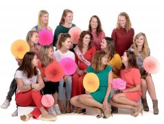Vrijgezelledag met 12 vrouwen allemaal om de bruid heen en kijken naar haar met zeer gekleurde kleding en waaiers in hun handen  gefotografeerd door fotograaf in de fotostudio Rotterdam  www.marijnissenfotografie.nl