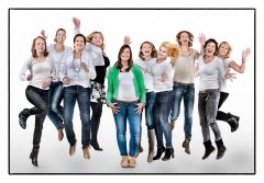 Vrijgezellenfeest, 9 dames springen in de lucht gekleed in spijkerbroek en wit shirt en de bruid staat in het midden in spijkerbroek en wit shirt met groen jasje waardoor de foto om haar draait gefotografeerd in de fotostudio Marijnissen fotografie Rotterdam. www.marijnissenfotografie.nl