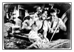 2 mandenmakers zitten in een fabriekje de een is bezig en de ander hangt half om zijn nek en lacht naar de camera gefotografeerd door Marijnissen Fotografie Rotterdam.. www.marijnissenfotografie.nl
